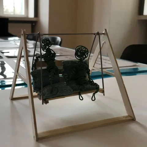 	Zwei Drahtfiguren sitzen auf einer selbstgebauten kleinen Hollywoodschaukel.