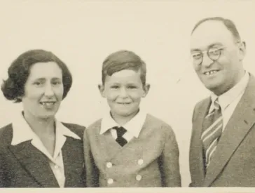 S-W-Bild. Stark vergilbt. Eine Frau, ein Kind und ein Mann in förmlicher Kleidung schauen freundlich in die Kamera. 