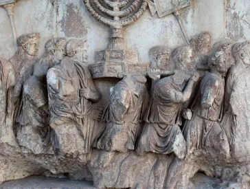 Beschädigtes Relief: eine Gruppe Männer trägt einen Chanukkaleuchter auf den Schultern.