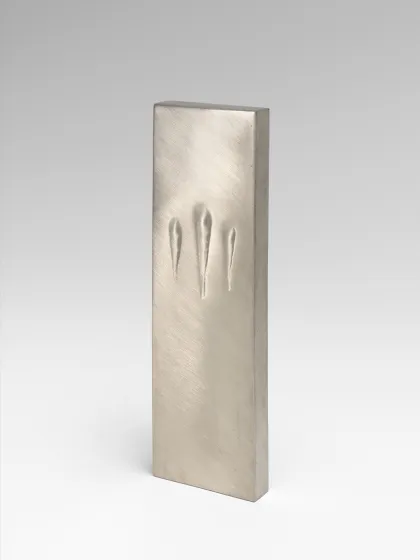Das Bild zeigt das Kunstwerk Touching Mezuzah von Sari Srulovitch. Die Mezuzah ist rechteckig und silberfarben und trägt drei Kerben.